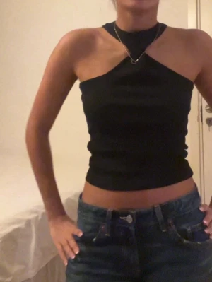 Svart  topp - Säljer en svart,  topp från Gina Tricot i storlek XS. Toppen har en unik asymmetrisk design med en axel bar och hög halsringning. Perfekt till jeans eller kjol. Aldrig använt, helt ny.