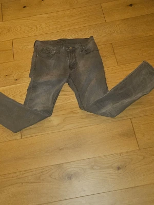 Gråa skinny jeans från Nudie Jeans - Säljer ett par gråa skinny jeans från Nudie Jeans i storlek W31 L32. Jeansen har klassisk femficksdesign, smal passform och är tillverkade i mjukt jeanstyg. Snygga detaljer på bakfickorna och diskret tvättad look. Lagats en gång nere vid gylfen men annars är de i gott skick
