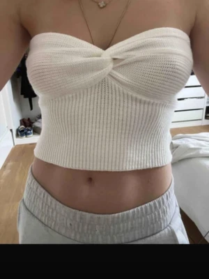 Vit ribbad bandeau tubtopp - Säljer en vit bandeau tubtopp i ribbat material med twistad detalj framtill. Toppen är axelbandslös och croppad, perfekt till sommaren. Mjuk och stretchig känsla som sitter snyggt på kroppen.