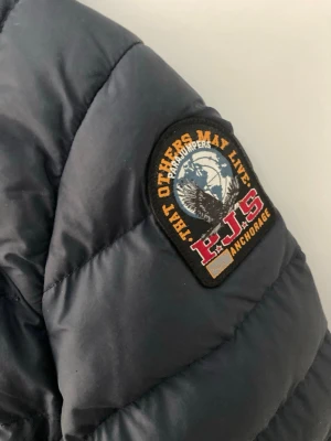 Mörkblå lättviktsdunjacka Parajumpers - Säljer en mörkblå lättviktsdunjacka från Parajumpers med huva och dragkedja framtill. Jackan har quiltad design, två sidofickor med dragkedja och den klassiska Parajumpers-loggan på ärmen. Perfekt för kyliga dagar och riktigt snygg streetstil. Liten lagning på ena armen som knappt syns när jackan är på. Se sista bilden. 