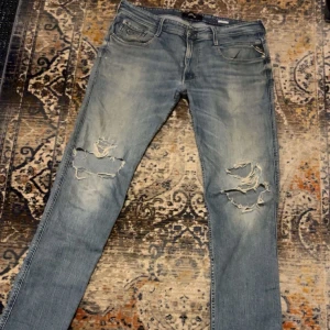 Replay Anbass ljusblå slitna jeans - Säljer ett par Replay Anbass jeans i ljusblå tvätt med slitningar och hål på båda benen. Klassisk femficksmodell med dragkedjegylf och snygga detaljer på bakfickorna. Perfekta för dig som gillar en avslappnad och trendig look. Midja 38 längd 34. Jätte fint skick 