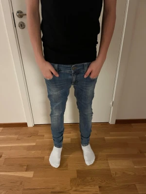 Blå slim jeans från Dondup - Säljer ett par blå skinny jeans från Dondup med klassisk femficksdesign och snygga slitningar på låren. Jeansen har låg midja och smal passform hela vägen ner. Materialet är mjukt jeans-tyg med stretch för extra komfort. Perfekta till sneakers eller boots.