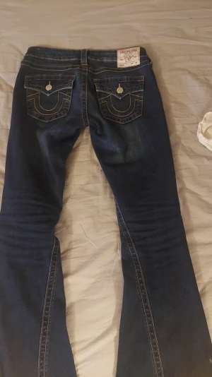 True Religion Joey Low Rise Flare Jeans - Säljer mina snygga mörkblå True Religion jeans i modellen Joey med låg midja och flare-ben. Riktigt snygga detaljer och skön passform. Säljer då de är lite stora. De är endast använda 3 gånger och är i mycket fint skick. 