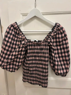 Rutig blus med puffärmar Boii - Supersöt blus med svart och rosa rutigt mönster och stora puffärmar. Smockad kropp som ger en tight passform och bred urringning. Från danska märket Boii. 