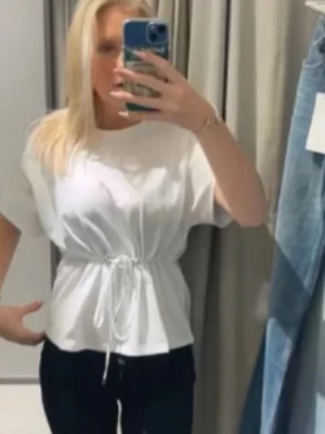 Vit blus med knyt i midjan - Säljer en fräsch vit blus med korta ärmar och snygg knytning i midjan som ger en fin siluett. Perfekt till jeans eller kjol för en clean look. Blusen är i mjukt bomullsmaterial och har en avslappnad passform.