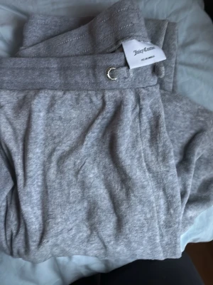Grå mjukisset från Juicy Couture - Säljer ett grå mjukisset från Juicy Couture med klassisk huva och dragkedja framtill. Koftan har ribbade detaljer och en liten metallring vid halsen. Perfekt för en chill och sportig look.