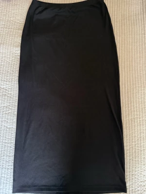 Svart ribbad långkjol  - En svart, ribbad långkjo. Kjolen har en rak och enkel siluett med stretchig midja och är gjord i mjukt material som sitter skönt. Perfekt att styla med sneakers eller boots för en clean look.