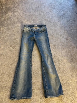 Blå bootcut jeans Gina Tricot XS - Säljer ett par blå bootcut jeans från Gina Tricot i storlek XS. Jeansen har klassisk femficksdesign, snygga detaljer på bakfickorna med knappar och broderi, samt en lätt tvättad look. Perfekta för dig som gillar retrovibbar och vill ha ett par jeans med lite vidare ben.
