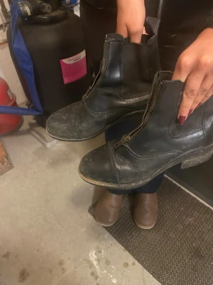 Svarta boots med dragkedja framtill - Säljer ett par svarta boots i skinn med grov sula och dragkedja framtill. Skorna har rund tå och låg klack, vilket ger en cool och robust look. Perfekta till jeans eller kjol för en edgy stil.