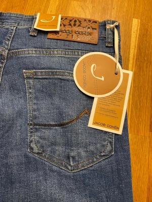 Blå jeans från Jacob Cohën - Snygga blå jeans från Jacob Cohën med klassisk femficksdesign och läderpatch med mönster bak i midjan. Jeansen har en rak passform och är tillverkade i mjukt denimtyg. Perfekta för dig som gillar stilrena och tidlösa jeans. 