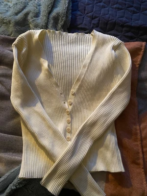Ribbad vit kofta med knappar !! - Snygg ribbad kofta i vit färg med djup V-ringning och långa ärmar. Koftan har flera små knappar framtill och är figurnära i modellen. Perfekt att styla med jeans eller kjol för en trendig look. Kommer inte ihåg vart den är ifrån men skulle tro att den är ifrån vero moda eller ginatricot🏷️*är i storlek M men skulle kunna passa någon med S, är också lite strechy*