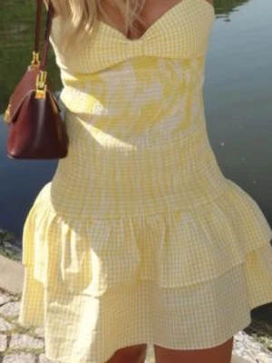 Gul- och vitrutad kort klänning - Söt kort klänning i gul- och vitrutigt mönster med volangkant och axelbandslös design. Klänningen har en feminin passform och är perfekt för varma dagar. Materialet känns lätt och luftigt, vilket gör den skön att bära under sommaren.