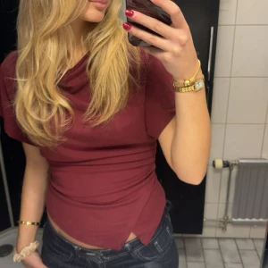 Vinröd tight topp med kort ärm - Säljer en vinröd topp med tight passform och korta ärmar. Toppen har en enkel design med rund halsringning och är gjord i ett stretchigt material som sitter snyggt på kroppen. Perfekt för dig som gillar stilrena och trendiga plagg.