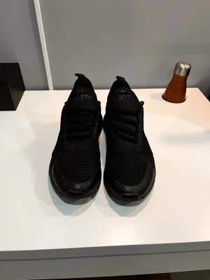 Nike Air Max 270 helsvarta sneakers - Säljer ett par helsvarta Nike Air Max 270 sneakers med luftig mesh-ovandel och synlig Air Max-dämpning i hälen. Skorna har en sportig design med svarta snören och diskret Nike-logga på sidan. Perfekta för dig som gillar stilrena och bekväma sneakers.