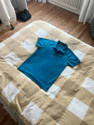 Blå pikétröja från Ralph Lauren - Snygg blå pikétröja från Ralph Lauren . Tröjan har knappar framtill och är tillverkad i mjukt bomullsmaterial. Perfekt för en avslappnad och stilren look.