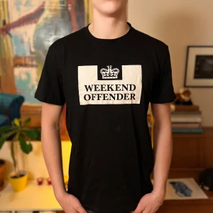 Svart t-shirt från Weekend Offender - Svart t-shirt med klassisk passform från Weekend Offender. Stor vit logga och text på bröstet. Rund halsringning och korta ärmar. Perfekt för en avslappnad stil.