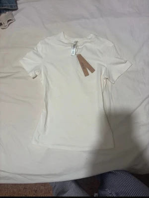 Vit t-shirt från SKIMS - En enkel och stilren vit t-shirt från SKIMS med rund hals och korta ärmar. T-shirten har en tight passform och är helt ny med prislappen kvar.