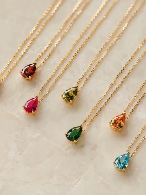 Ett guldpläterad halsband  - Snyggt halsband med droppformad sten i olika färger, inspirerat av månadsstenar som granat, ametist, smaragd och safir. Perfekt för att matcha din födelsedagsmånad eller favoritfärg. Stenen sitter i en elegant infattning som ger ett lyxigt intryck.