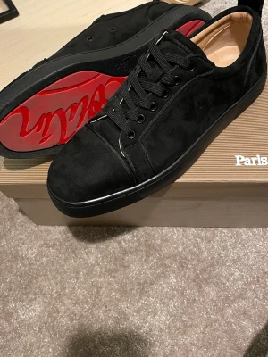 Svarta sneakers från Christian Louboutin - Stilrena svarta sneakers i mocka från Christian Louboutin med klassisk röd sula och svarta skosnören. Låg modell med diskreta detaljer och exklusiv känsla. Perfekta för dig som vill sticka ut med en lyxig touch.