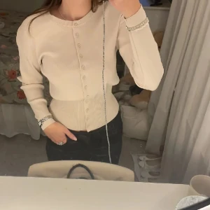 Beige kofta med tajt midja zara - Snygg beige kofta med rund hals och knäppning framtill. Tröjan har långa ärmar och ribbade muddar vid ärmslut och midja. Perfekt att styla med jeans eller kjol för en clean look.