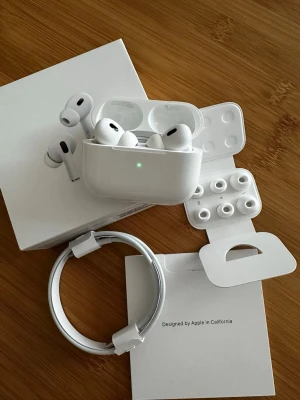 Apple AirPods Pro 2  trådlösa hörlurar helt nya - Säljer ett par vita Apple AirPods Pro med laddningsetui, extra silikonpluggar och laddningskabel. Hörlurarna har en stilren och kompakt design i plast och levererar grymt ljud med brusreducering. Perfekt för musik, poddar och samtal.