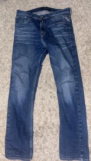 Blå Replay jeans med raka ben - Snygga blå jeans från Replay med klassisk femficksdesign och raka ben. Jeansen har diskreta slitningar och detaljerade sömmar, samt Replay-logga på fickan. Perfekta för en avslappnad och trendig look.