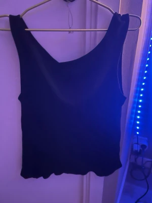 Svart ärmlös linnetopp - En enkel och stilren svart linnetopp med breda axelband och rundad halsringning. Toppen är ärmlös och har en rak passform, perfekt att matcha med jeans eller kjol. Materialet känns mjukt och stretchigt.