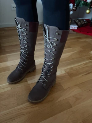 Bruna höga snörstövlar från Timberland - Snygga bruna höga stövlar från Timberland med snörning hela vägen upp och rund tå. Tillverkade i mocka med detaljer i mörkare brunt upptill. Perfekta för dig som vill ha en robust och stilren look. Som nya använda ett fåtal ggr!