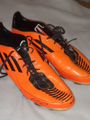 Adidas F50 orange fotbollsskor - Säljer ett par Adidas Adizero F50 F30 fotbollsskor i en riktigt snygg orange färg med svarta detaljer och svarta snören. Skorna har klassisk låg profil och mönstrad sula för bra grepp på planen. 