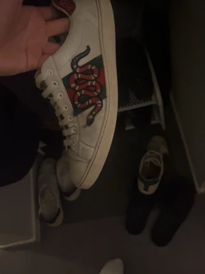 Gucci Ace snake - Säljer ett par vita Gucci Ace sneakers i läder med den ikoniska gröna och röda sidoremsan och broderad orm. Skorna har lågt skaft och klassisk siluett, med gröna detaljer på hälen. Perfekta för dig som vill sticka ut med lyxig streetstyle.