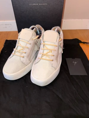 Beige sneakers från Giuseppe Zanotti - Snygga beige sneakers från Giuseppe Zanotti med vita sulor, ljusa snören och dragkedjor på sidorna. Skorna har en stilren design med detaljer i mocka och canvas, samt logga på plösen. Perfekta för dig som vill ha något unikt och trendigt storlek 40 passar 42.