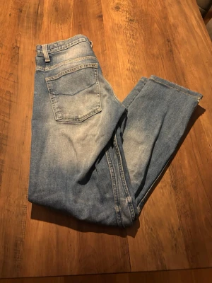 Blå raka slim jeans från Crocker jeans  - Klassiska blå jeans från Crocker Jeans i modellen 310 slim med raka ben och normal passform. Jeansen har en ljus tvätt med snygga slitningar på låren och är tillverkade i robust denim. Perfekta för en avslappnad och tidlös stil. Dom är i bra skick med det finns ett litet hål längst ner på ett utav benen(se bild).
