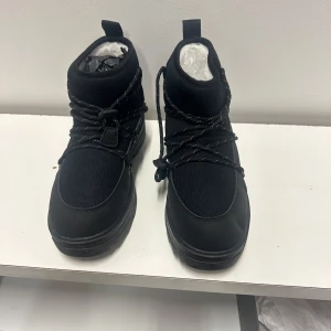 Svarta kängor från Tretorn med snörning 40 - Snygga svarta kängor från Tretorn storlek 40 med grov sula och snörning framtill. Ovandelen är i en mix av textil och syntetmaterial, vilket ger en sportig och modern look. Perfekta för dig som gillar streetstyle och vill ha något bekvämt och stilrent.