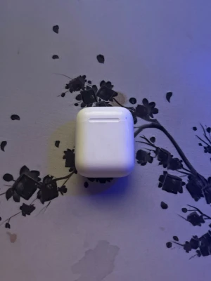 Vitt laddningsetui till Apple AirPods - Säljer ett vitt laddningsetui till Apple AirPods. Etuiet är tillverkat i blank plast och har en kompakt, fyrkantig form med rundade hörn. Perfekt för att ladda och förvara dina trådlösa hörlurar smidigt.