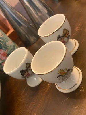 Söta äggkoppar med barnmotiv - Tre vita äggkoppar i porslin med gulliga barnmotiv och tunna gulddetaljer längs kanterna. Perfekta till frukostbordet för dig som gillar retro eller samlar på unika köksprylar.