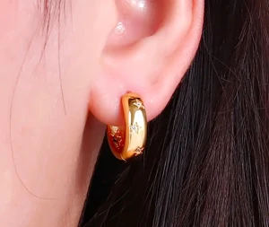 Guldiga örhängen med stjärndetaljer - Säljer ett par chunky, guldiga hoops med ingraverade stjärnor och små glittriga stenar. Örhängena har en rund, bred form och ger en cool och trendig vibe. Perfekt för dig som gillar att sticka ut med detaljer som syns. Kommer med söt förvaringspåse med blommönster.