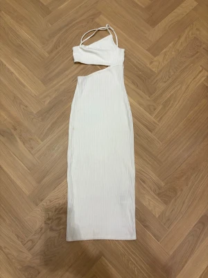 Vit omlottklänning från H&M Divided - Säljer en vit ribbad långklänning från H&M Divided i storlek XXS. Klänningen har ett coolt asymmetriskt snitt med omlott-detalj och cut-out vid midjan. Axelbandslös på ena sidan och smala axelband på andra ger en trendig look. Perfekt för dig som gillar minimalistisk stil.