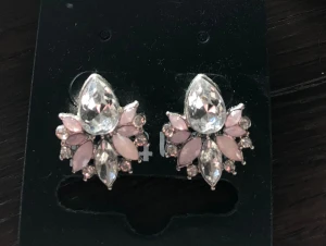 Glittriga örhängen med rosa stenar - Säljer ett par snygga örhängen med stora droppformade glittriga stenar i mitten och ljusrosa detaljer runt om. Örhängena har en silverfärgad bas och är perfekta för att ge din look extra bling. Passar dig som gillar statement-smycken och glittriga accessoarer.