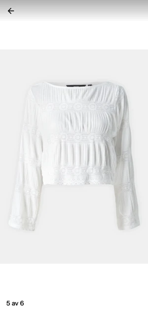 Vit blus med spets från Vero Moda - Superfin vit blus från Vero Moda med långa ärmar och broderade spetsdetaljer i blommönster. Blusen är croppad och har en luftig, lätt struktur i bomull. Perfekt för dig som gillar romantisk och boho-inspirerad stil!