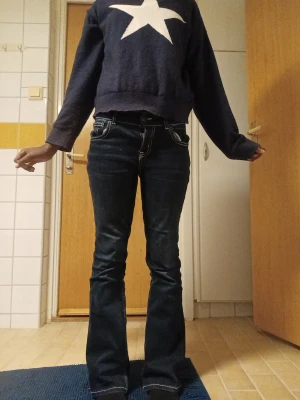 Lager 157 Popular Stitch – Bootcut jeans 160 (XS–S), mörkblå - Snygga mörkblå stich midrise bootcut jeans från 157 med kontrasterande vita sömmar och klassiska fem fickor. Jeansen har en knappstängning och detaljerad bakficka med lock och knapp. Perfekt för dig som gillar retrovibbar och stilren denim.