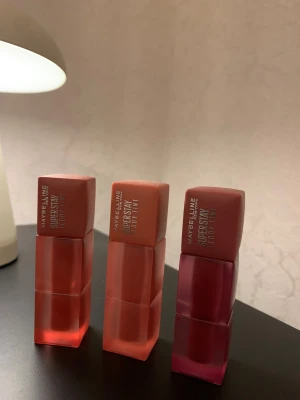 Maybelline SuperStay Teddy Tint läppfärger - Alla 3 är endast testade fåtal gånger. Iprincip som nya! Nypris för 1 var 170kr. Tre Maybelline SuperStay Teddy Tint läppfärger i nyanserna 15 Skinnydip (ljus korall), 10 Current Mood (varm nude) och 55 Kneehigh (djup bärig röd). Snygga fyrkantiga förpackningar i matt plast med färgmatchad design. Perfekt för dig som gillar pigmenterade läppar. 