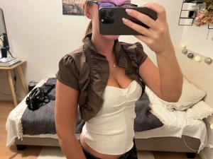 Brun bolero - En  kort brun bolerotopp med puffärm och volangkant. Perfekt för dig som vill ha en trendig och chic look.