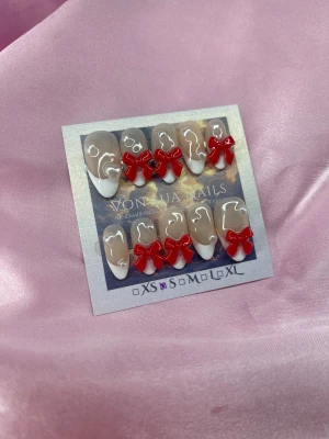 RedBows (S);Medium Almond - Snygga press on-naglar i en medium mandelform med nude bas, handmålade vita franska tippar och 3D-detaljer i form av röda rosetter och vita pärlhjärtan. Perfekt för dig som vill ha en söt och trendig look. Kommer i S: 15 mm, 11,5 mm, 12 mm, 11 mm, 9 mm 
