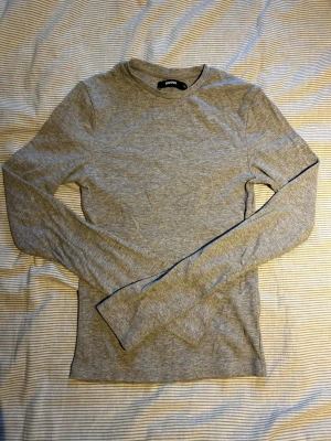 Grå ribbad långärmad tröja Bik Bok - Superskön grå långärmad tröja från Bik Bok i ribbad bomull. Enkel och stilren med rund hals och slim passform, perfekt att ha till jeans eller under en jacka. Passar dig som gillar basic och comfy vibes.