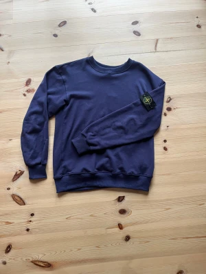 Mörkblå Stone Island sweatshirt M - Snygg mörkblå sweatshirt från Stone Island i storlek M. Tröjan har klassisk rund hals, ribbade muddar och den ikoniska Stone Island-patchen på vänster ärm. Tillverkad i mjuk bomull som är skön mot huden. Perfekt för dig som gillar streetwear och stilrena plagg.