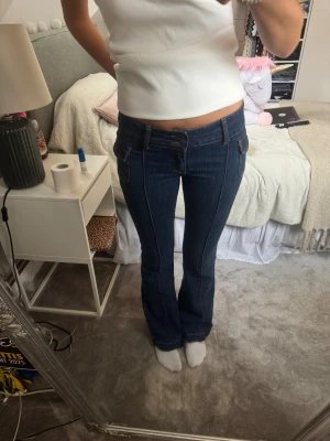 Mörkblå bootcut jeans med låg midja - Snygga mörkblå jeans med bootcut och låg midja. Jeansen har dubbla knappar, framfickor och markerade sömmar längs benen. 