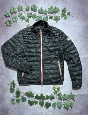 Moncler Daniel Puffer Jacket Size 2 (S) [ÄKTA] - 🎨 Färg: Svart med röd vit dragkedja 📏 Storlek: Moncler storlek 2, motsvarar Small (S) ♻️ Skick: 10/10 Mycket fint begagnat skick – inga synliga skador, fläckar eller slitage 🧵 Material: Lättviktsdun / quiltat yttertyg (typisk dun- eller syntetfyllning)