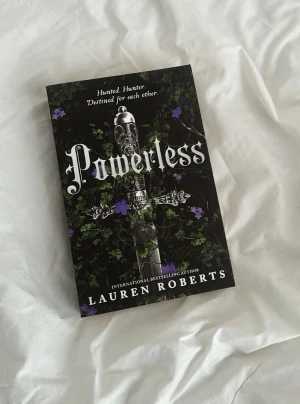 Powerless - En internationell bästsäljare med ett mystiskt omslag prytt av ett svärd och slingrande växter. Texten 'Hunted. Hunter. Destined for each other.' antyder spänning och öde. Perfekt för dig som gillar episka berättelser och dramatik.