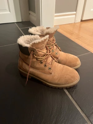 Timberland boots med foder strlk 39 - Snygga Timberland boots i beige mocka med mörkbrunt skaft och grov sula. Insidan är fodrad med mjuk päls för extra värme. Klassisk snörning med metallöglor och rund tå. Perfekta för kalla dagar.
