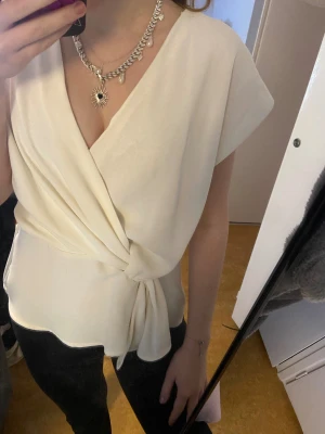 Vit omlottblus med knyt från Zara - Säljer en stilren vit blus från Zara i omlottmodell med v-ringning och knyt i midjan. Blusen har korta ärmar och är gjord i ett mjukt, lätt material som faller snyggt. Fin fest topp i storlek S.